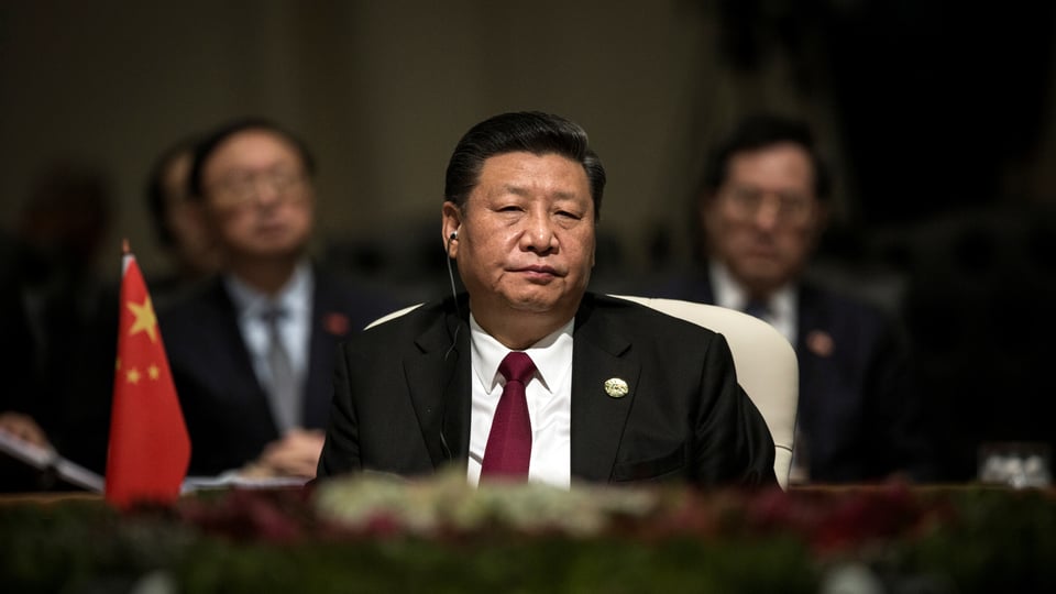 Xi sitzt an einem Tisch, neben ihm eine chinesische Tischflagge.