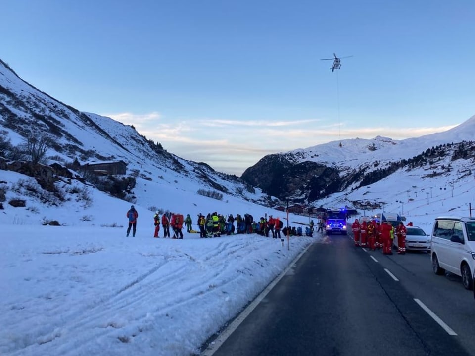 Rettungshelfer sind in Lech nach einem Lawinenabgang im Einsatz, ein Helikopter kreist am Himmel.