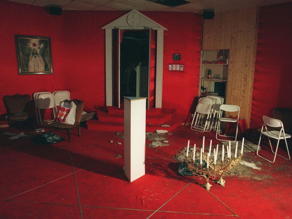 Raum mit roten Wänden und rotem Boden. Darauf liegen Kerzen und stehen mehrere Stühle.