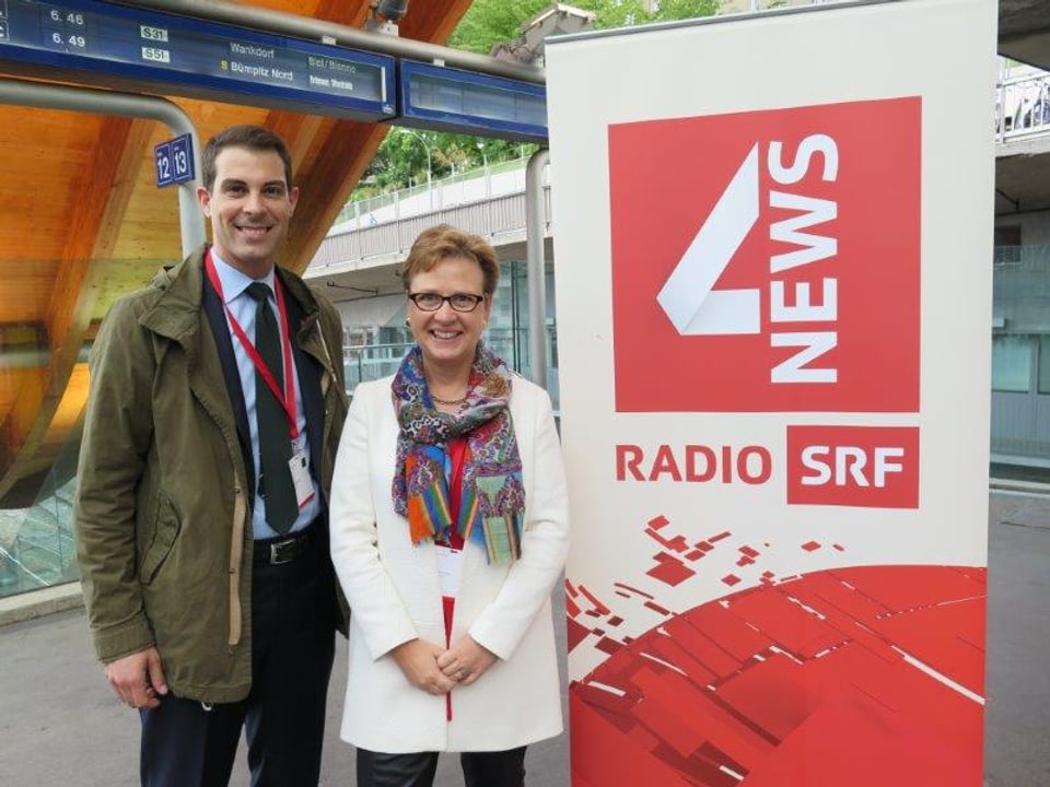 Thierry Burkart und Edith Graf-Litscher stehen lächelnd neben einem Plakat, auf dem «Radio SRF 4 NEWS» steht.
