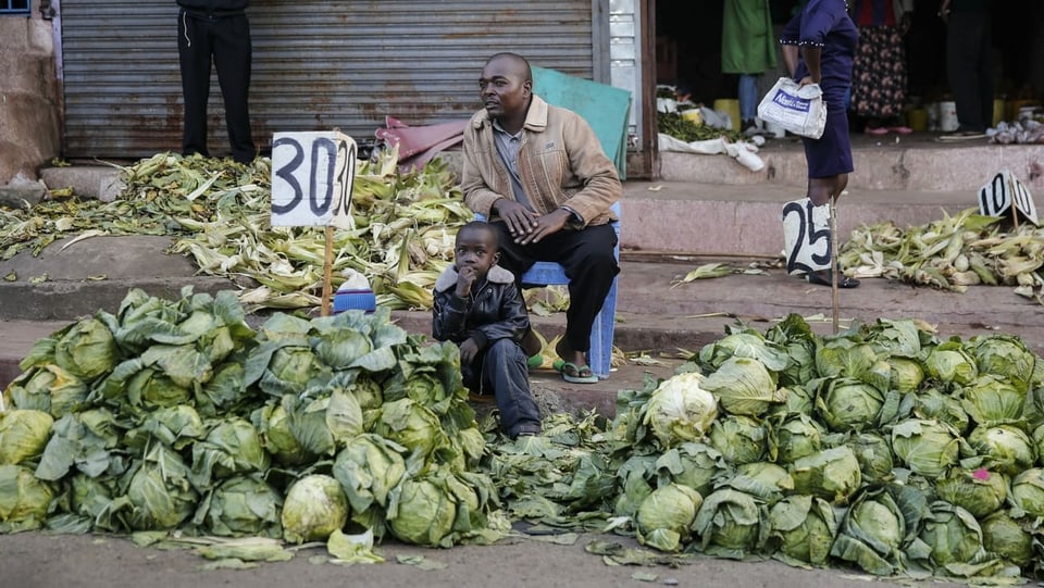 Ein Mann mit einem Kind verkauft Kohl vor einem geschlossenen Markt