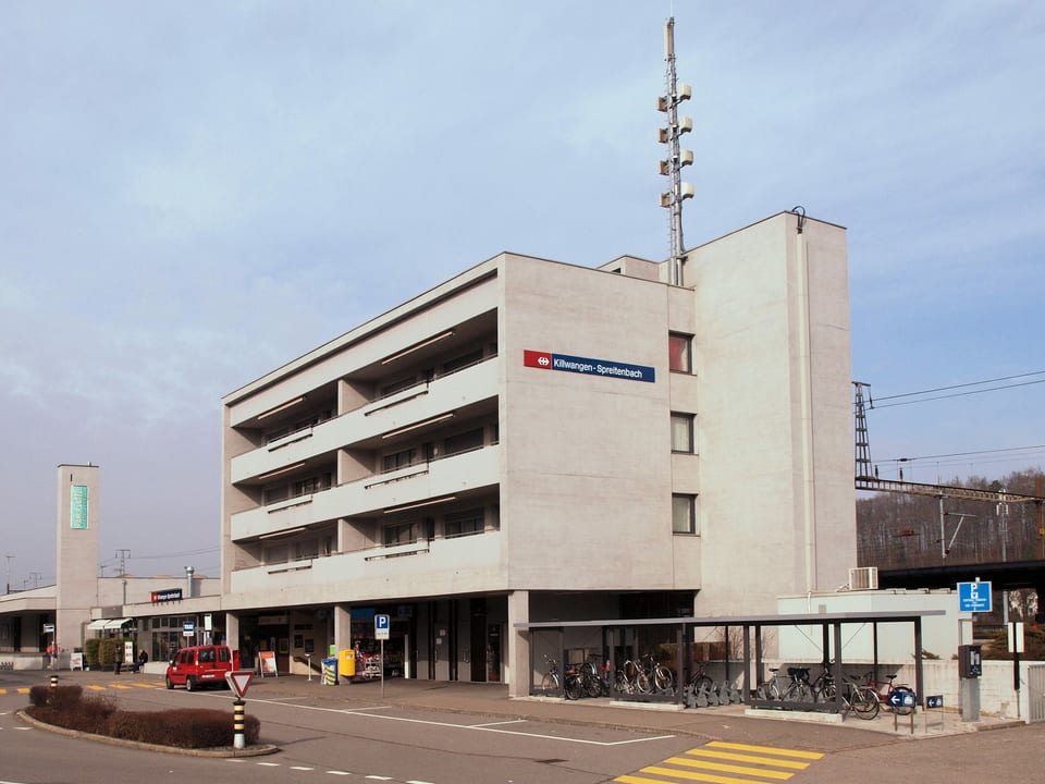 Ein Bahnhofsgebäude, das würfelförmig aus Beton gebaut ist. Es ist das Bahnhofsgebäude von Killwangen-Spreitenbach