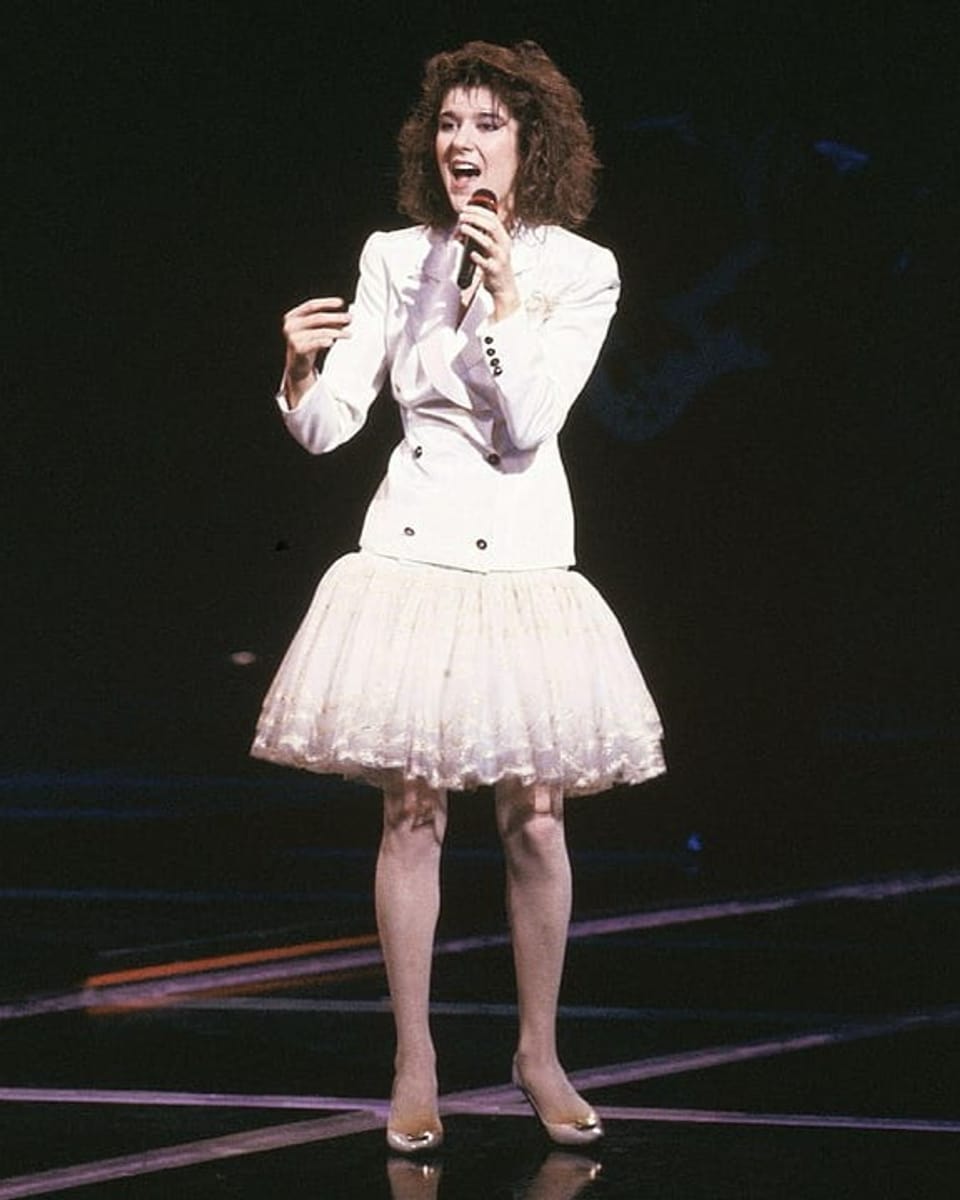 Eine junge Frau in weissem Rock steht mit einem Mikro auf der Bühne und singt.