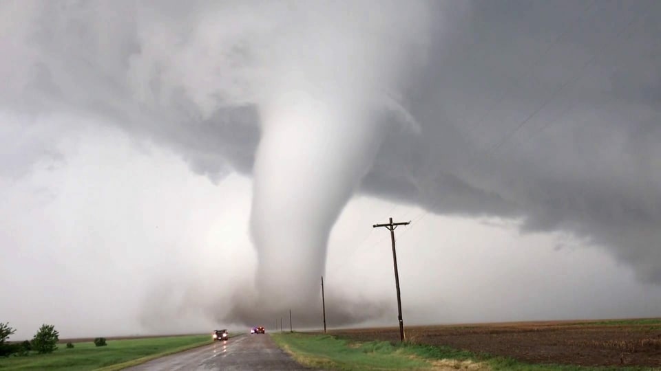 Naturkatastrophen wie Tornados haben enorme Zerstörungskräfte. Ein Tornado im Hintergrund, eine Strasse und 2 Autos im Vordergrund.