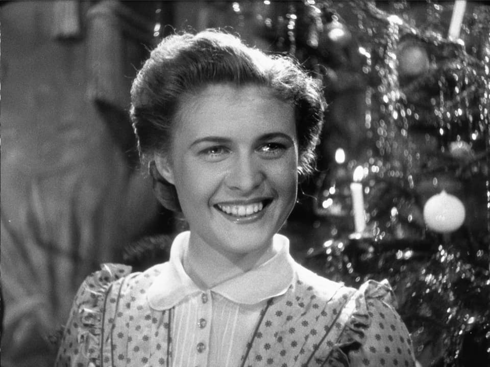 Grossaufnahme einer lächelnden Frau (Gilberte) mit Weihnachtsbaum im Hintergrund