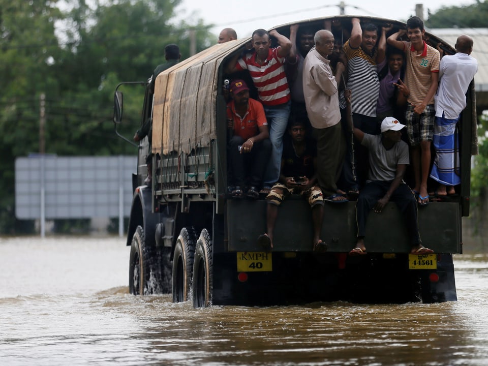 Menschen werden in einem Lastwagen durch eine überflutete Strasse abtransportiert. 