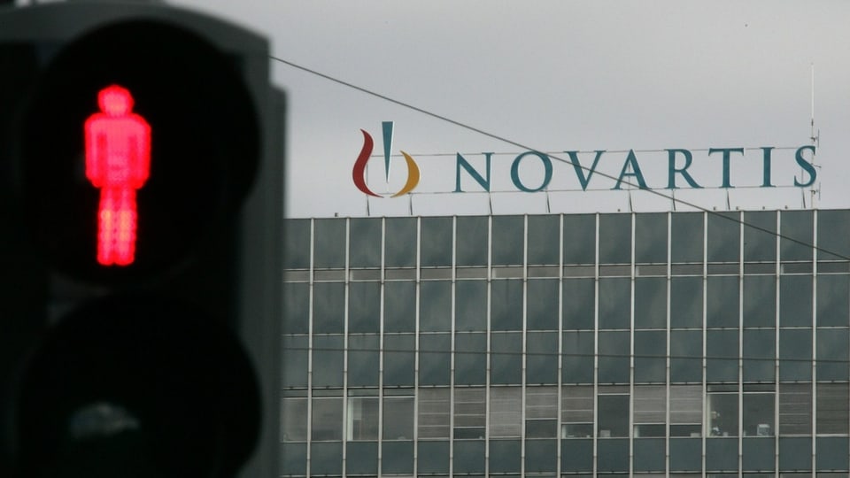 Novartis-Gebäude mit Schriftzug hinter Lichtsignal, das auf Rot steht