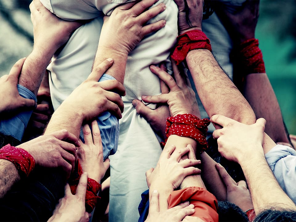 Viele Hände greifen zusammen und stützen eine Person.