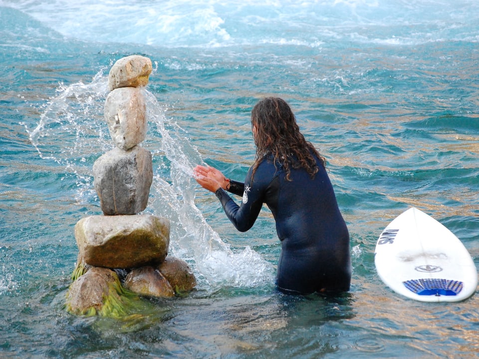 Mann im Neopren-Anzug bespritzt ein Steinmannli im Wasser