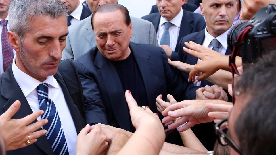 Ein zerknirschter Berlusconi inmitten von Bodyguards und Menschen, die ihm die Hand schütteln wollen.