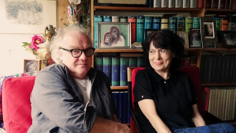 Ein Mann und eine Frau auf roten Sesseln vor einer Bücherwand.
