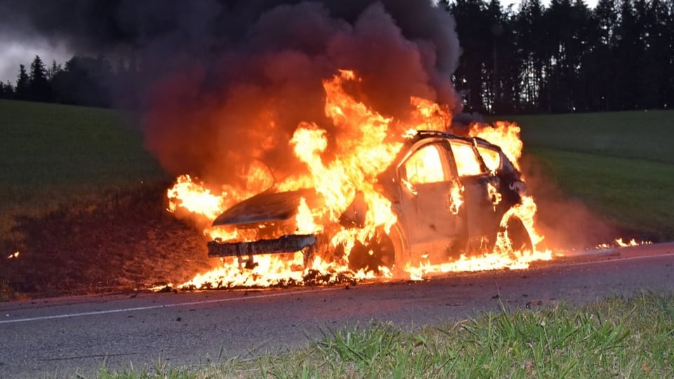 Graues, verbranntes Auto steht auf einer Strasse. Es ist dunkel.