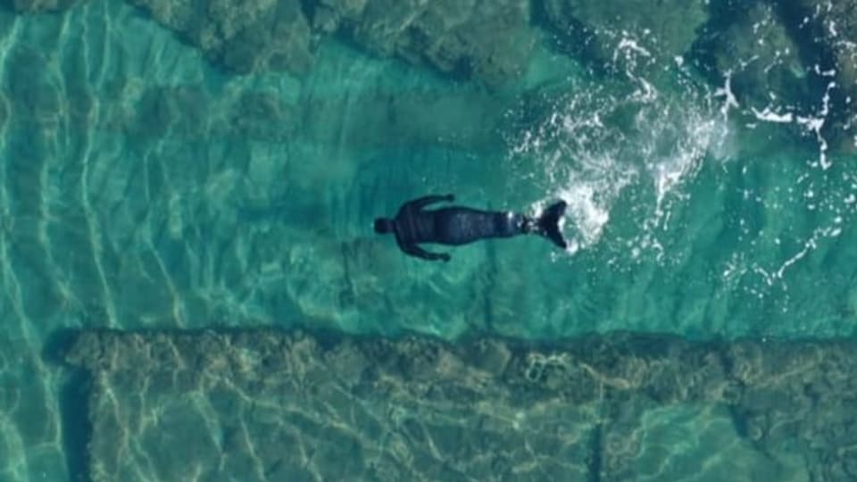 Mensch im Meerjungfrau-Kostüm schwimmt durch hellblaues Meerwasser