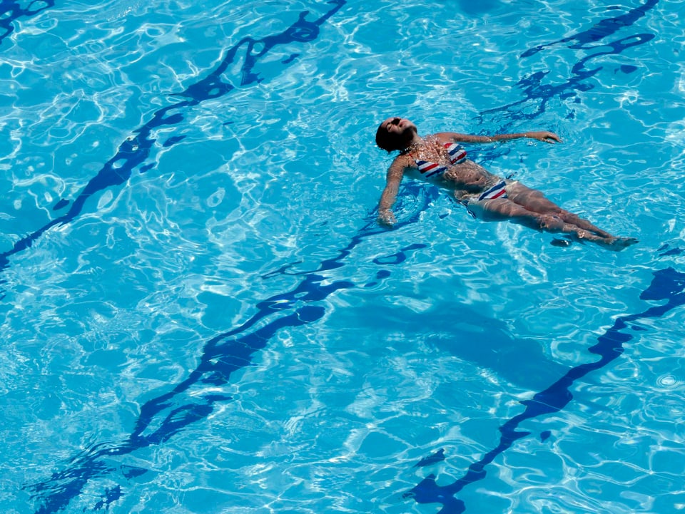 Frau lässt sich ein einem Pool auf dem Rücken treiben.