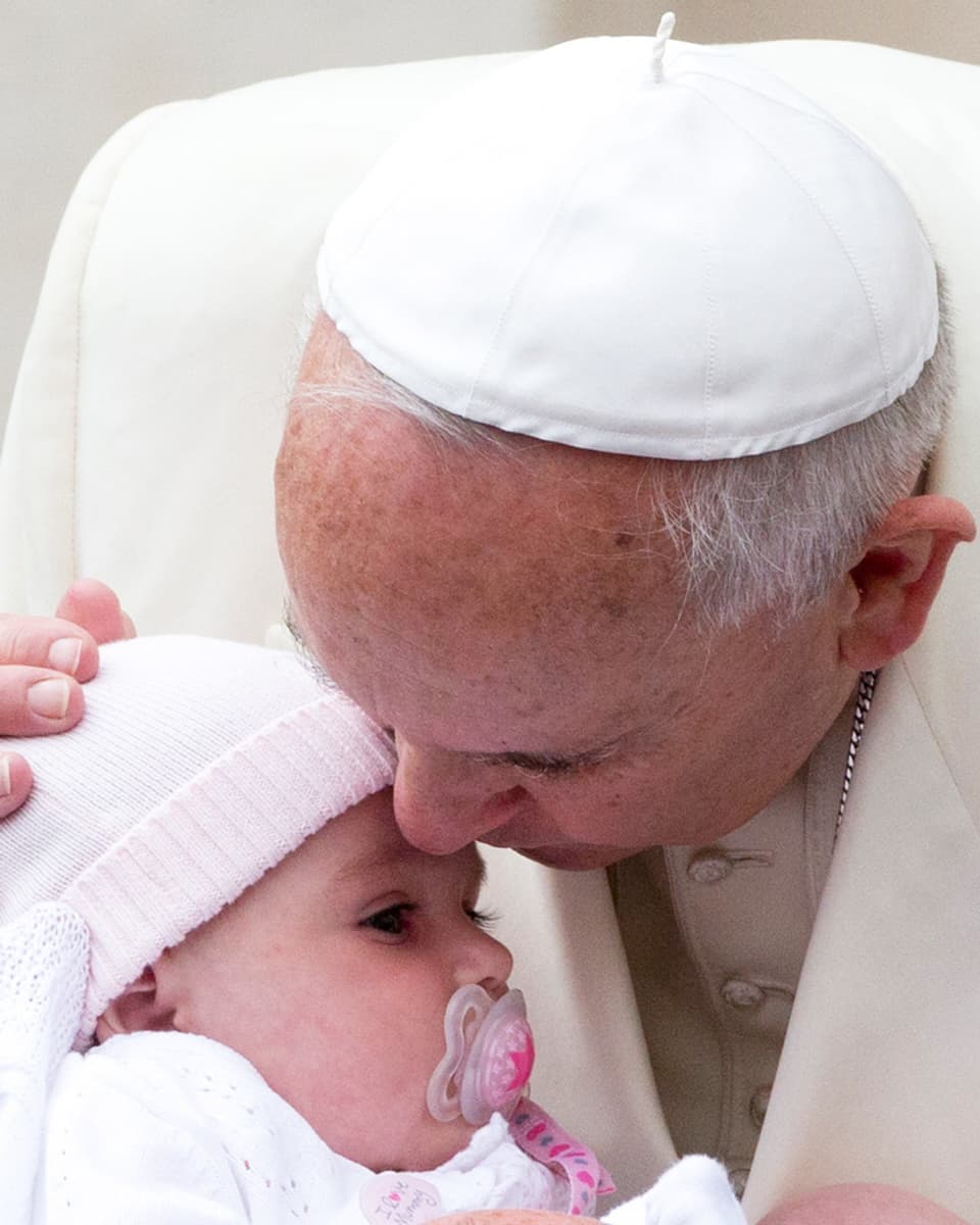 Der Papst küsst ein schnullerndes Kind.