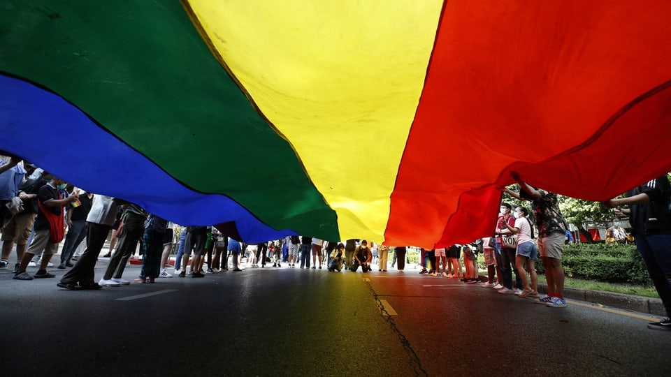 Bild unterhalb der Regenbogen-Flagge aufgenommen. Sichtbar sind die Beine der Teilnehmer.