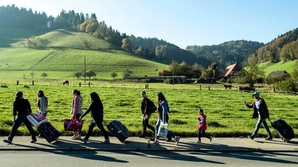 Asylbewerber aus Syrien mit Rollkoffern laufen durch die Emmentaler Landschaft.