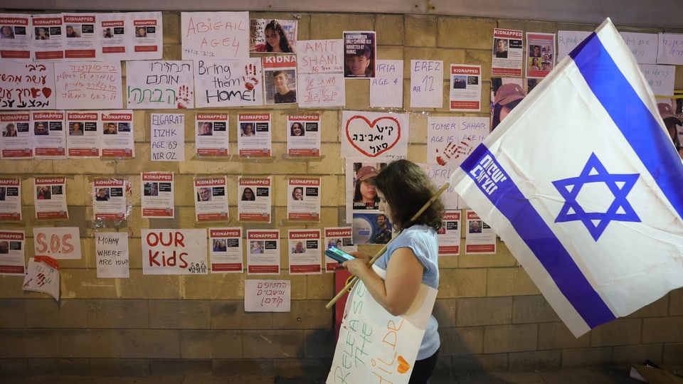 Wand mit Fotos, eine junge Frau mit Israel-Fahne davor.