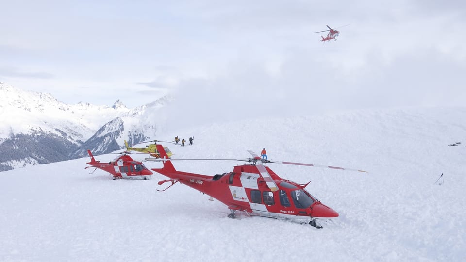 Zwei rot-weisse Rega-Helikopter auf einem Schneefeld.
