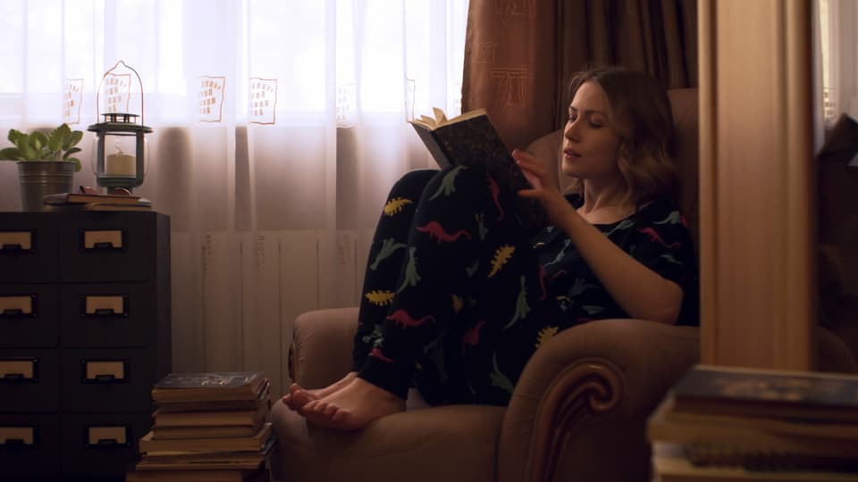 eine junge Frau sitzt im Pyjama auf einem Sessel und liest