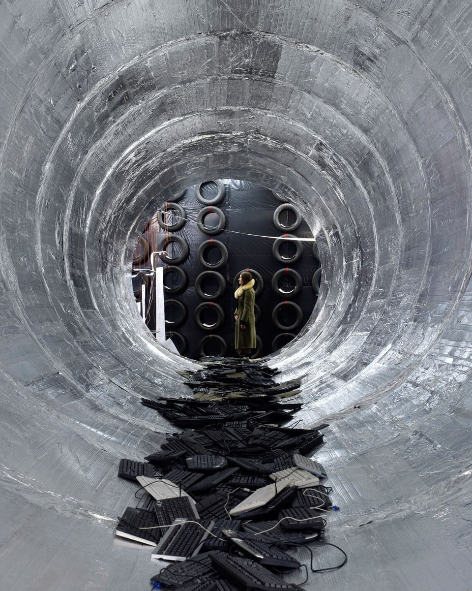 Ein metallener Tunnel, in dem gebrauchte Tastaturen liegen, zeigt an deren Ende eine Frau.