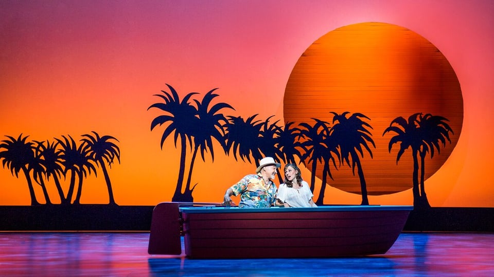 Ein Paar im Ruderboot, dahinter Palmen und ein Sonnenuntergang