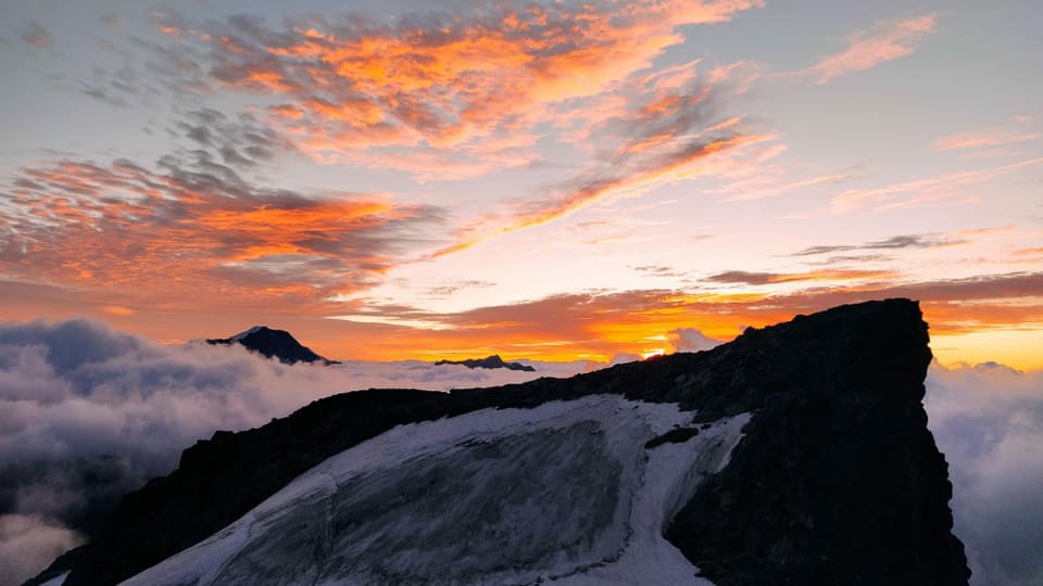 Sonnenaufgang auf dem Allalinhorn. Links und rechts unten brodelnde Quellwolken, darüber orange hohe Wolken.