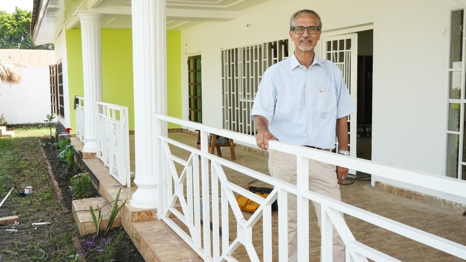 Eine Person steht auf einer Veranda eines Hauses im kolonialen Stil.