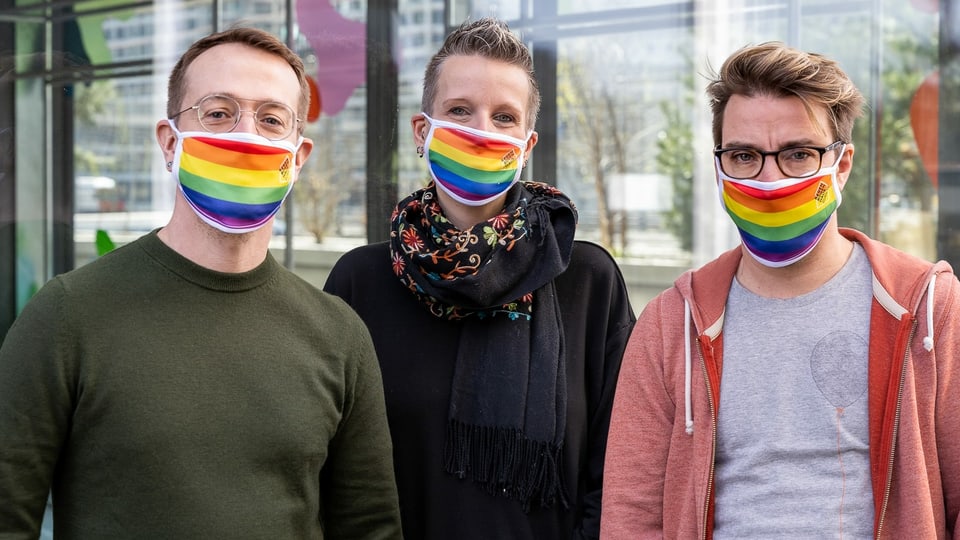 drei Menschen tragen Mundschutzmasken in Regenbogenfarben