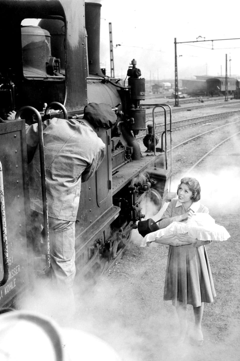 Eine Frau mit einem Säugling im Arm verabschiedet sich von einem Mann, der im Zug davon fährt.
