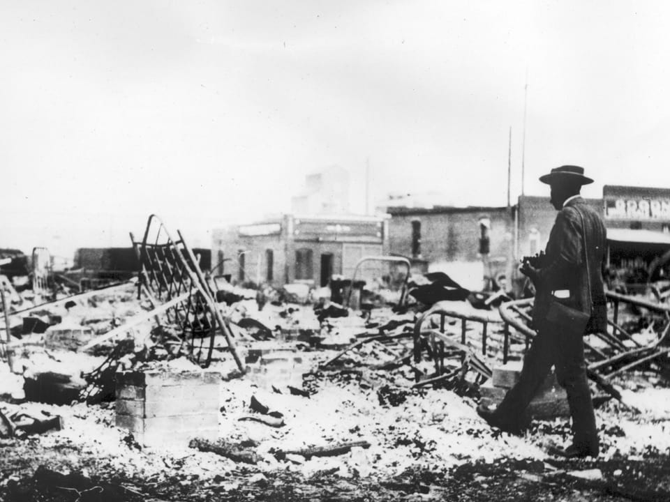 Ein schwarzer Mann mit Anzug und Hut stapft durch die Trümmer eines Hauses