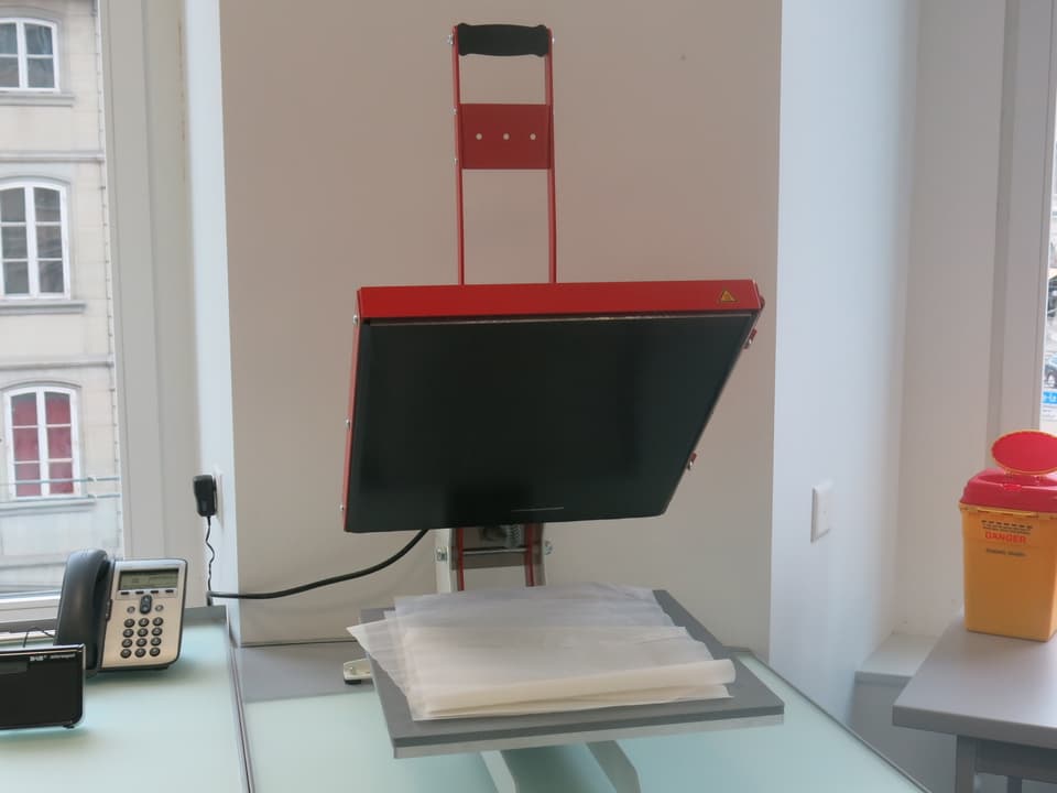 Ein rotes Gerät, ähnlich einem Waffeleisen, mit Papier drunter.