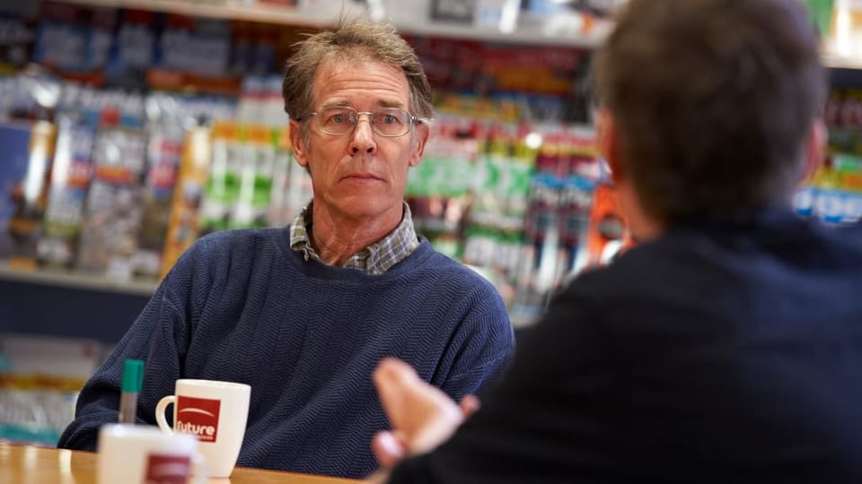 Mann mittleren Alters im Gespräch vor einer Bücherwand.