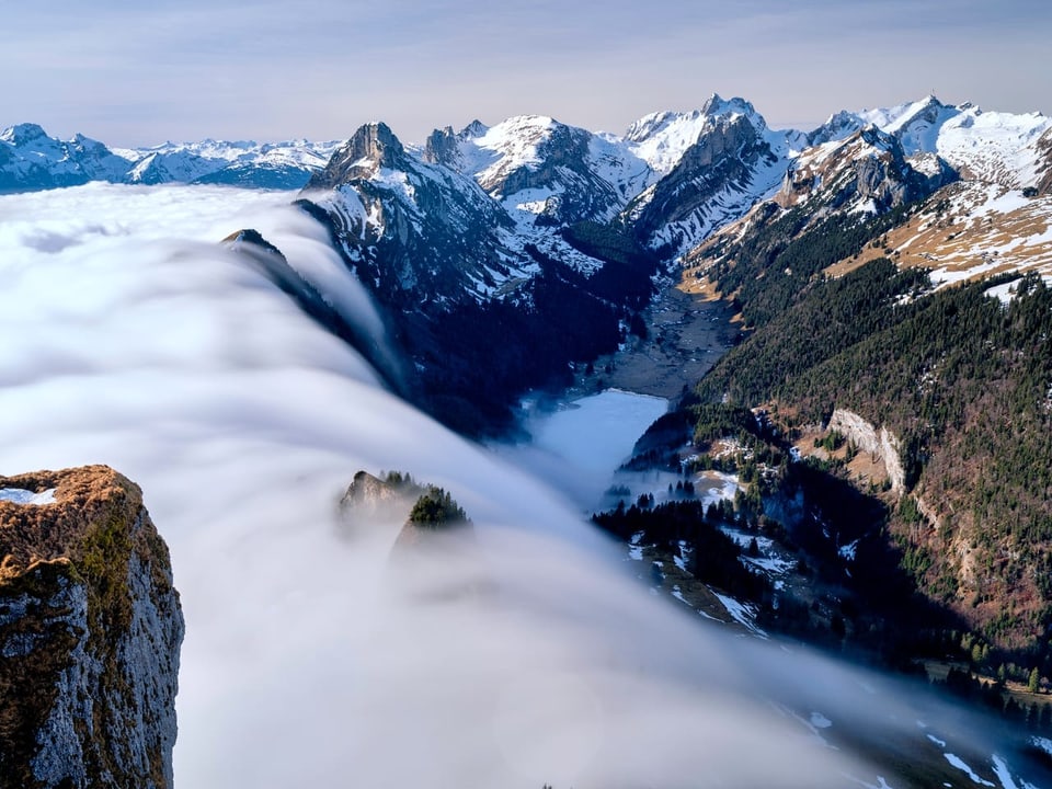 Berge mit zwei Tälern. Nebel strömt von der einen auf die andere Seite und erinnert an einen Wasserfall.
