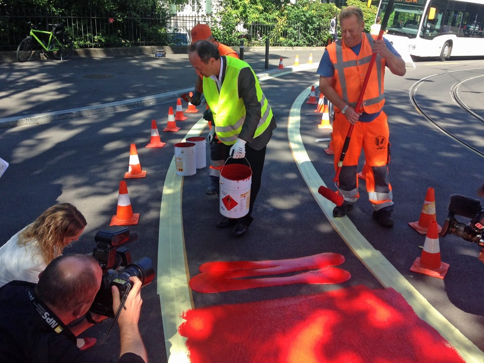 Stadtrat Richard Wolff bückt sich zu den roten Farbtöpfen, um einen Velostreifen an der Leonhardstrasse einzufärben.