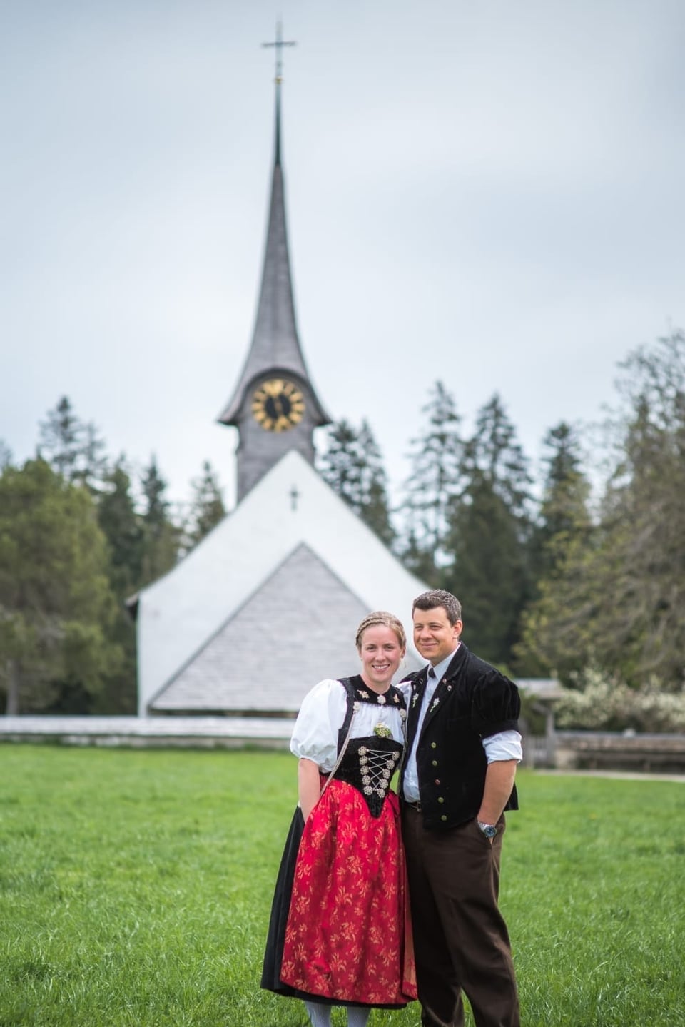 Ein Paar steht in einer Tracht vor einer Kirche.
