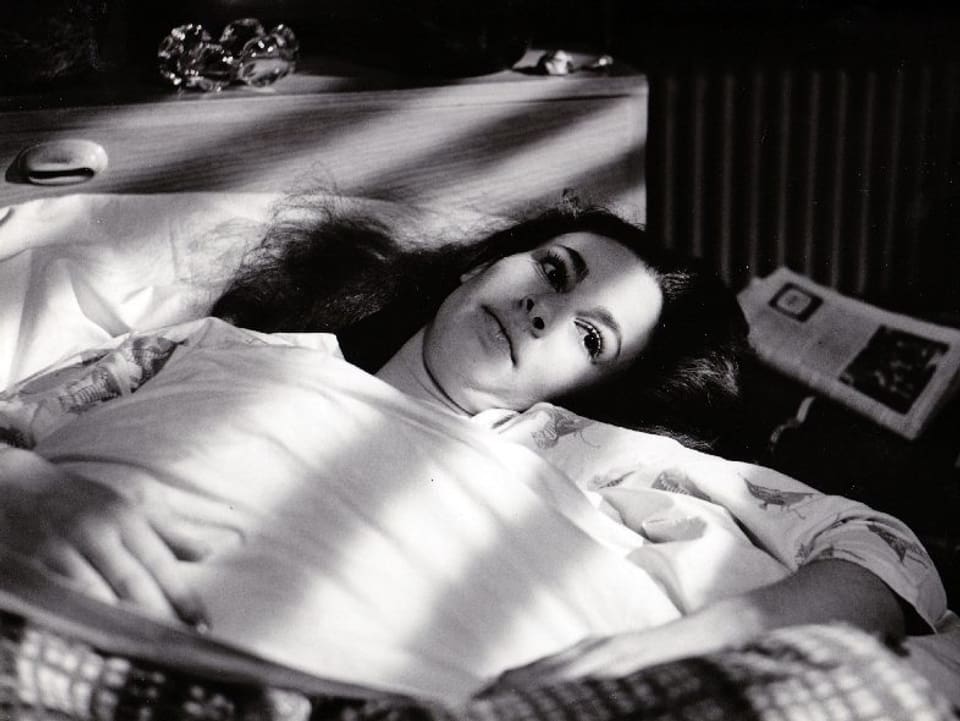 Eine Frau liegt auf einem Bett und blickt zur Decke.