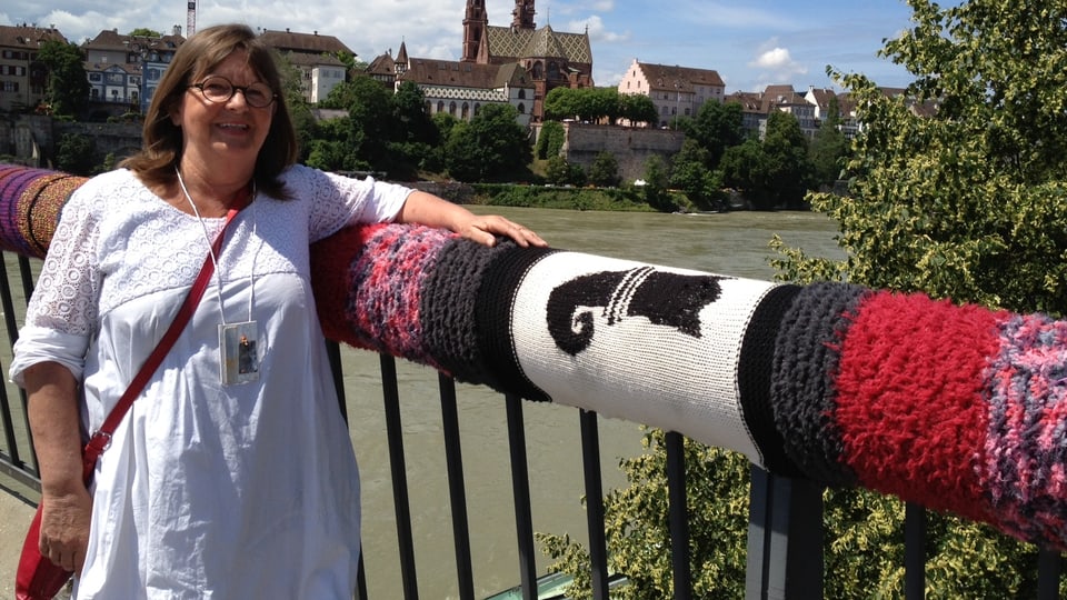 Kathrin Stalder vor dem eingestrickten Geländer der Wettsteinbrücke. Im Hintergrund der Rhein und Münster.