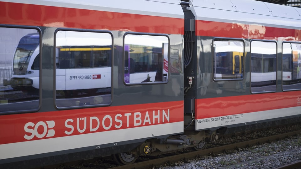 Ein Zug der Südostbahn steht auf einem Gleis. In den Fenstern spiegelt sich ein Zug der SBB.