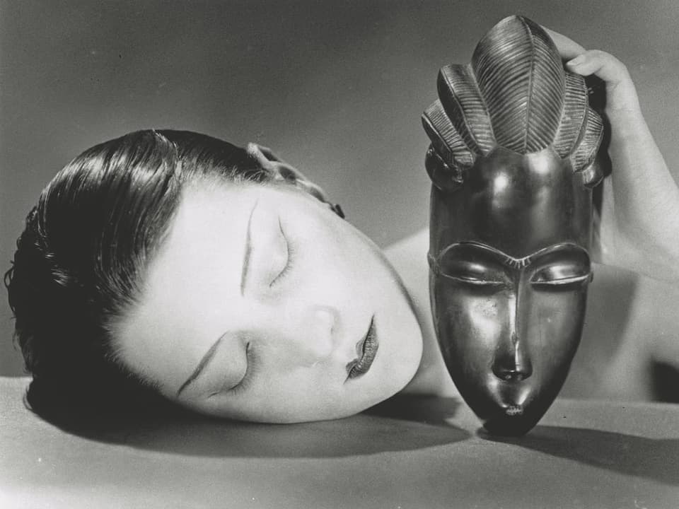 Ein schwarz-weisses Foto, links ein Frauengesicht mit geschlossenen Augen, rechts eine Holzmaske, auch Augen zu.
