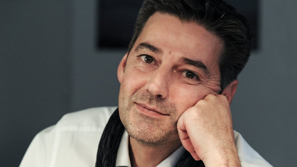 Andreas Neeser, mit weissem Hemd und dunklem Schal, blickt mit aufgestütztem Kopf in die Kamera.