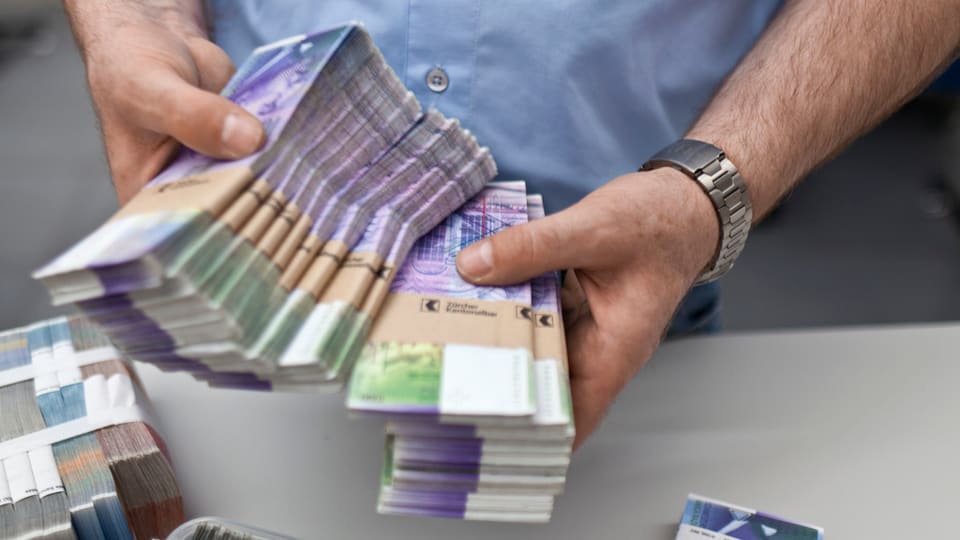 Ein Mann hält mehrere Bündel mit Tausend-Franken-Noten. 