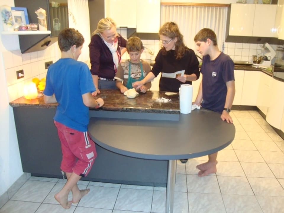 Katia Ambrosini mit drei von ihren Söhnen am Zopf backen. Sprachlehrerin Antje Skodock schaut zu und animiert die vier sich in Deutsch zu unterhalten. Treccia heisst Zopf.