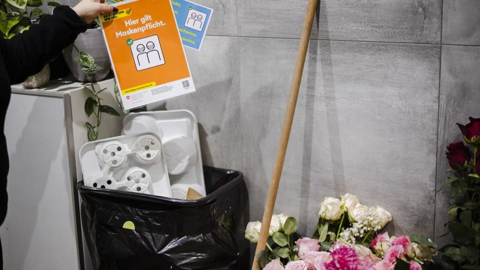 Eine Mitarbeiterin eines Blumengeschäfts wirft Hinweisschilder zur Maskenpflicht in den Abfall.