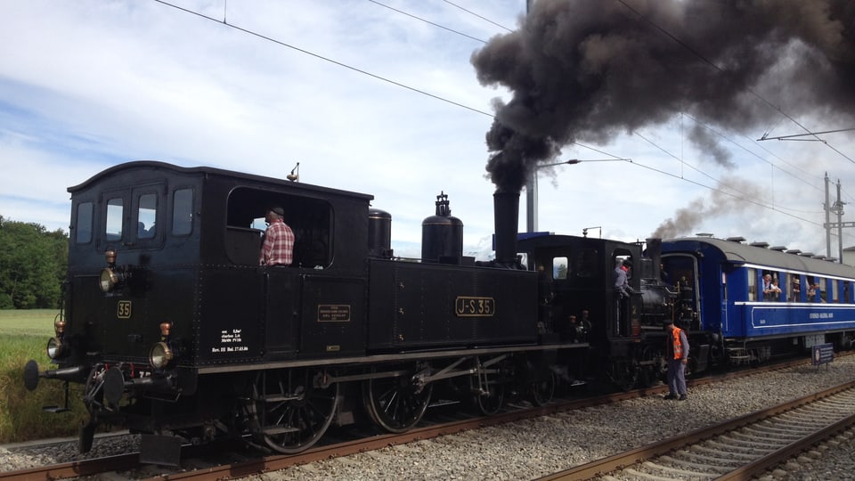 Zwei Dampflokomotiven ziehen einen blauen Wagen