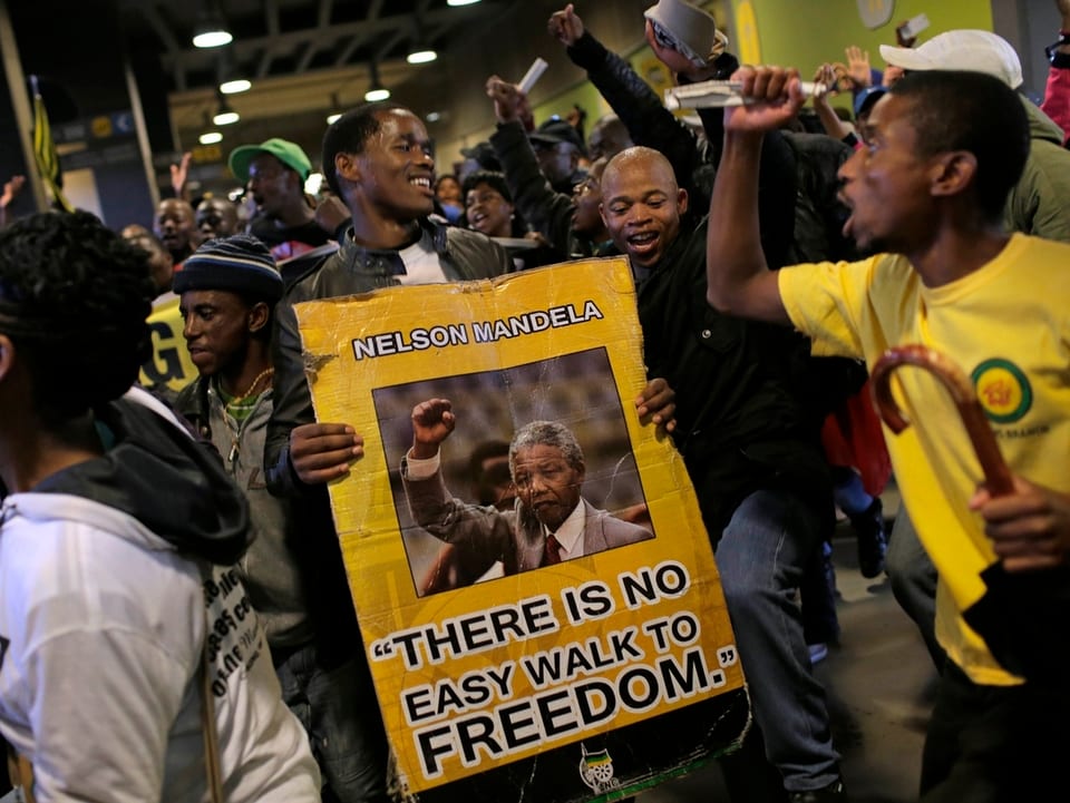 Menschen mit Mandela-Plakat in den Händen skandieren Parolen.