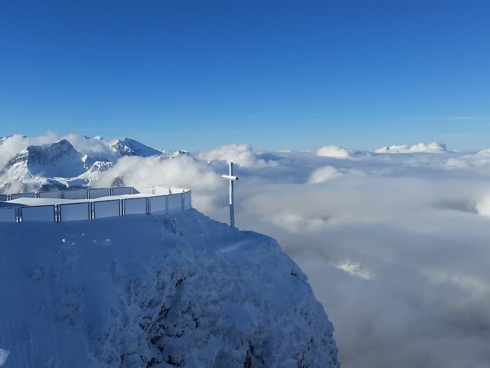 Verschneite Felsen, verschneites Gipfelkreuz und Nebelmeer.