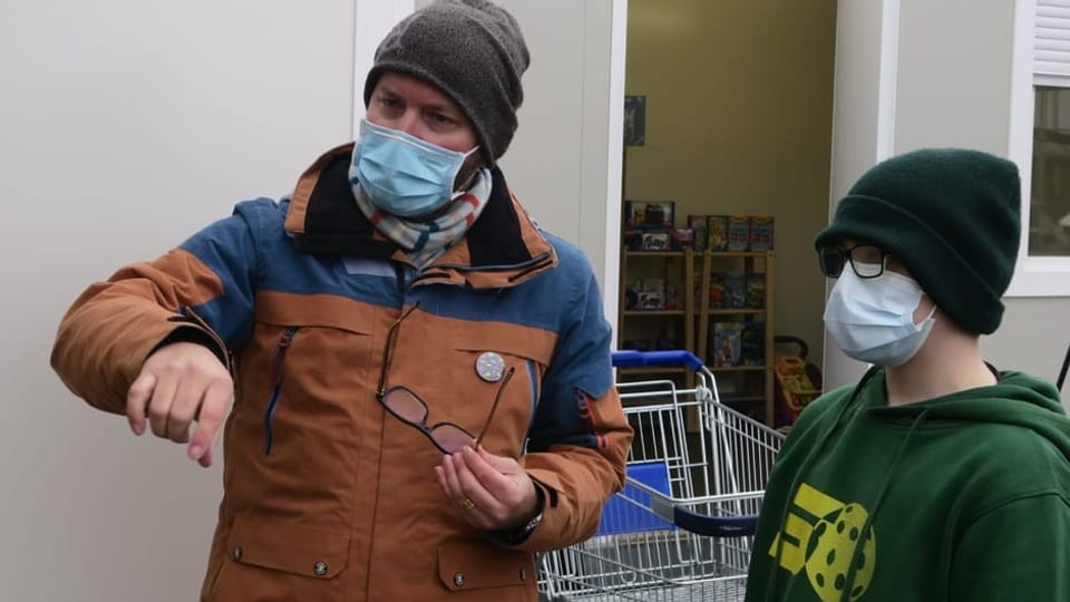 Zwei Personen stehen vor einem Container und sprechen miteinander.