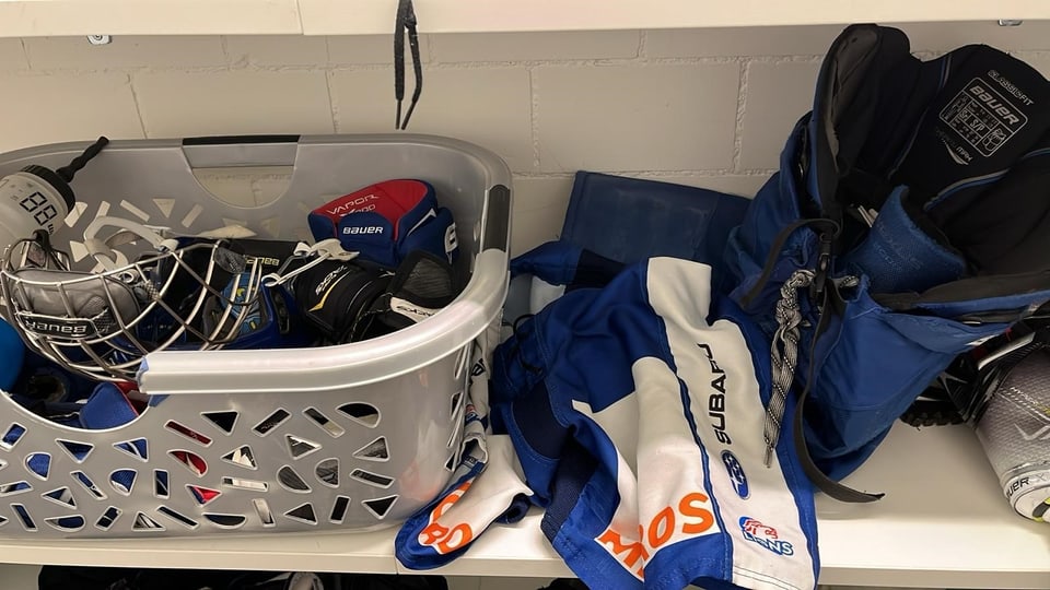 Eishockeyausrüstung mit Helm, Trikot, Hosen und Handschuhen auf einem Regal oder im Wäschekorb.