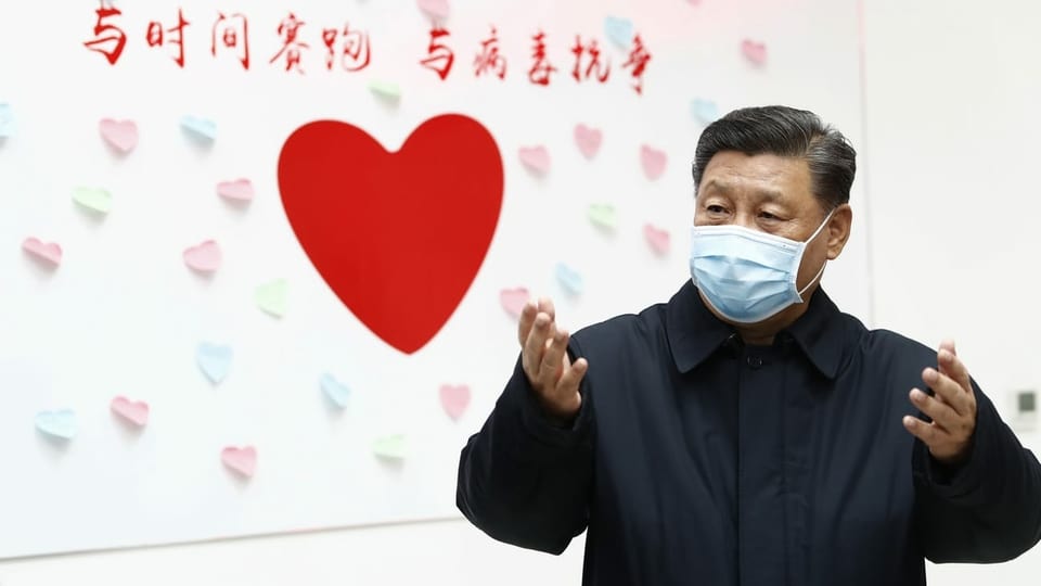 Xi Jinping mit Gesichtsmaske vor einem roten Herzen an der Wand.